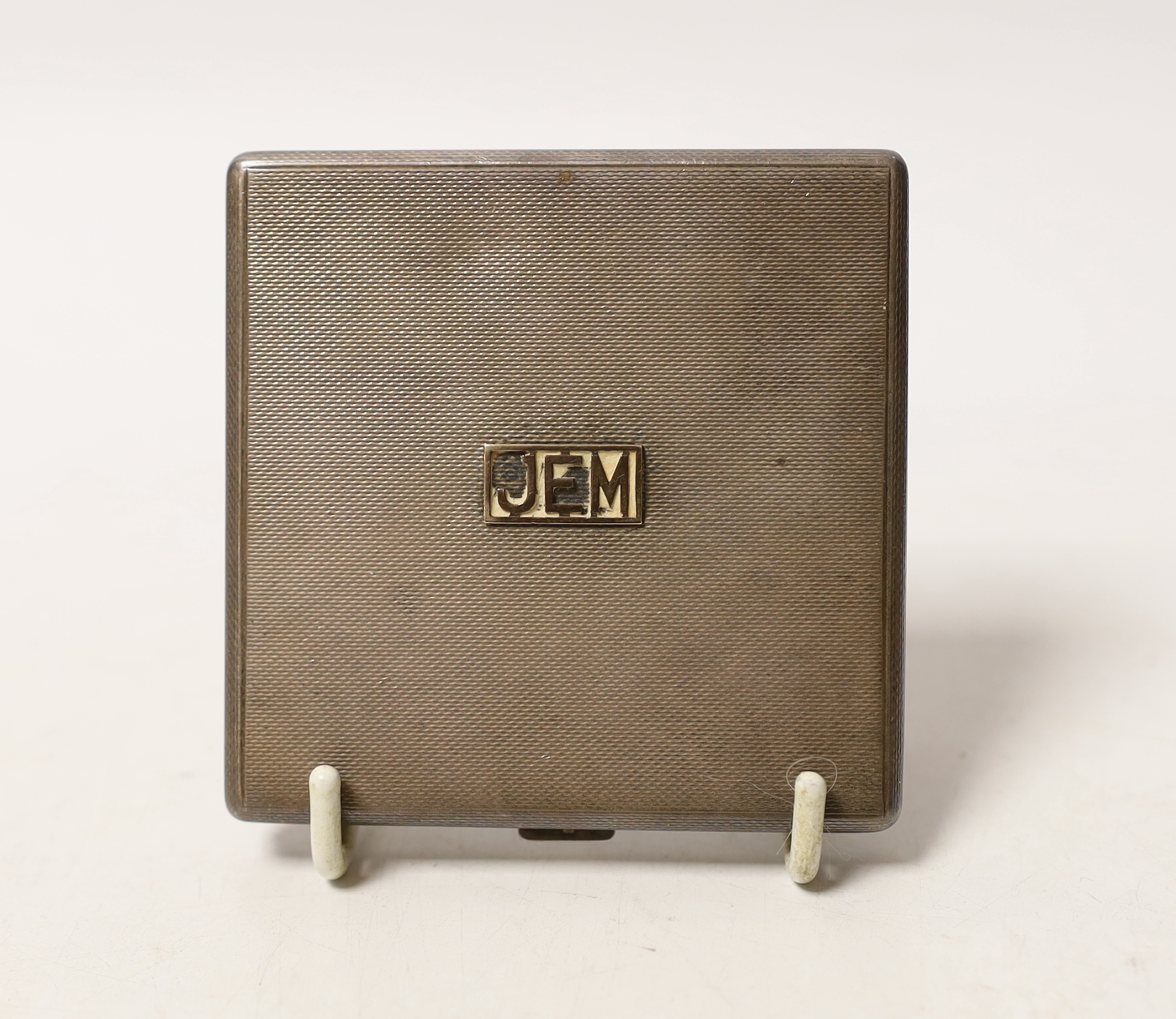 An Elizabeth II engine turned silver square compact, with applied yellow metal initials, 'JEM', W.H. Manton Ltd, Birmingham, 1961, 76mm.